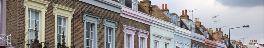 A row of terraced houses with painted stucco fronts in pale pink, cream and blue, stepping down a London street.
