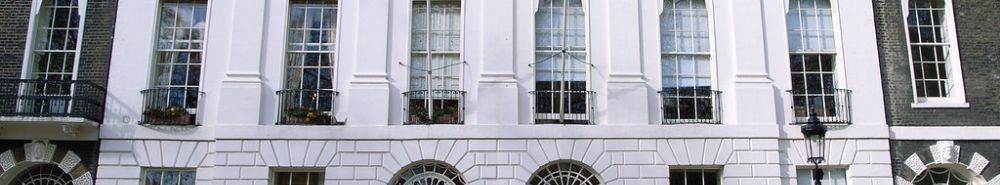 A white stucco terrace with tall sash windows, iron balconies and arched openings at street level.