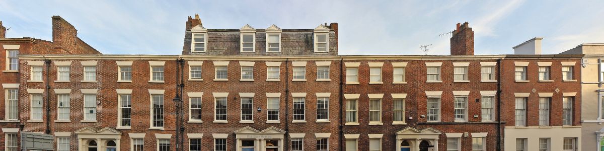 A long brick terrace of Georgian townhouses with sash windows and stone lintels, photographed from across the street.