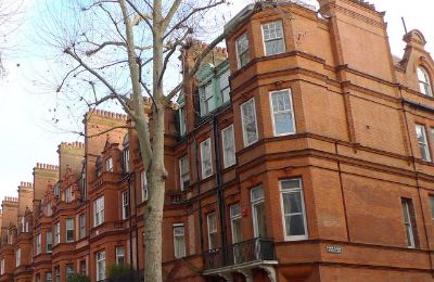 A red-brick mansion block of flats with bay windows and tall chimneys, seen from the pavement.